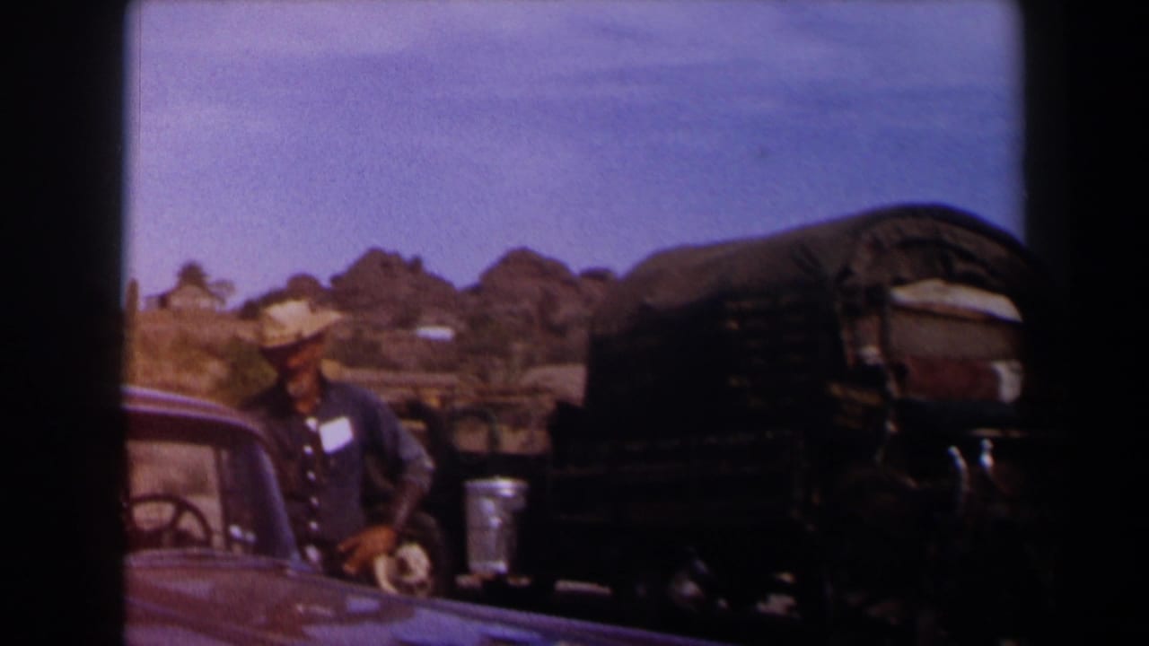 1958 Texas 8mm frame showing a cowboy-hatted man near a covered wagon, mule team area, and partial car in a desert setting.