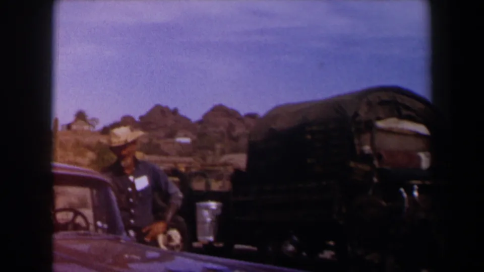 1958 Texas 8mm frame showing a cowboy-hatted man near a covered wagon, mule team area, and partial car in a desert setting.