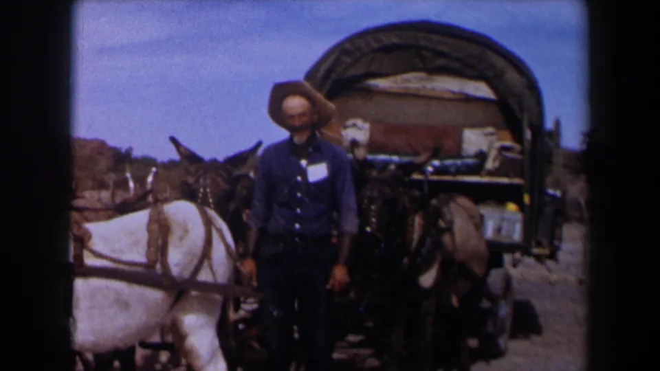 1958 Texas 8mm frame with a cowboy-hatted man standing close to a covered wagon and mule team in a dry landscape.