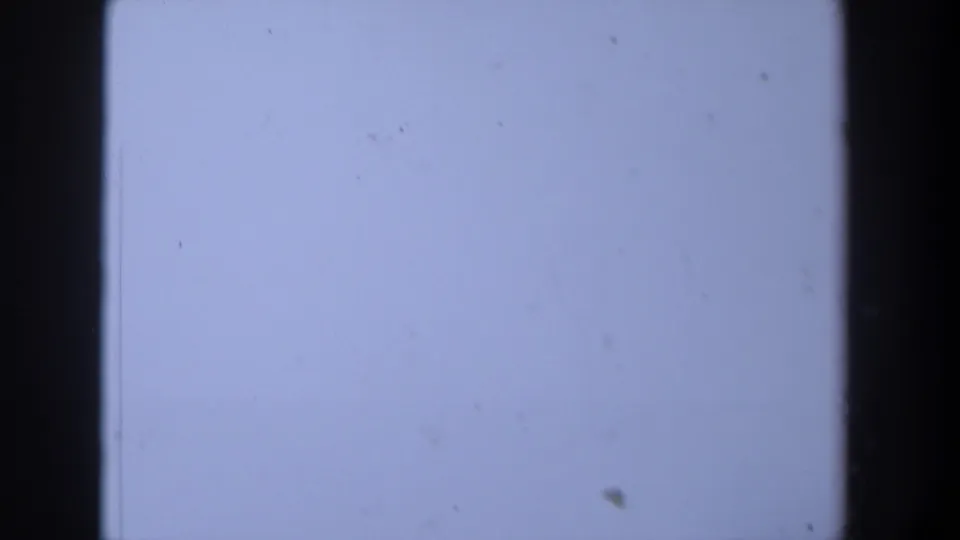 1958 Texas 8mm frame showing a light blue-white blank area with dark film borders, dust particles, and faint scratches.