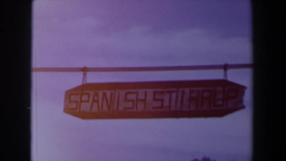 1958 Texas home-movie frame with the Spanish Street sign centered against sky, bordered by dark film edges.