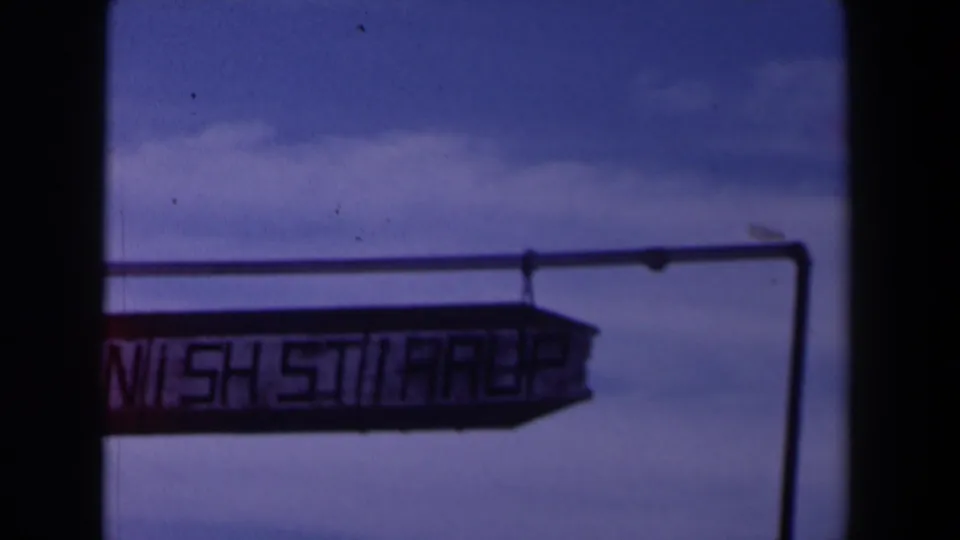 1958 Texas frame showing a partly cropped Spanish Street sign below a support rail, with blue sky and clouds above.