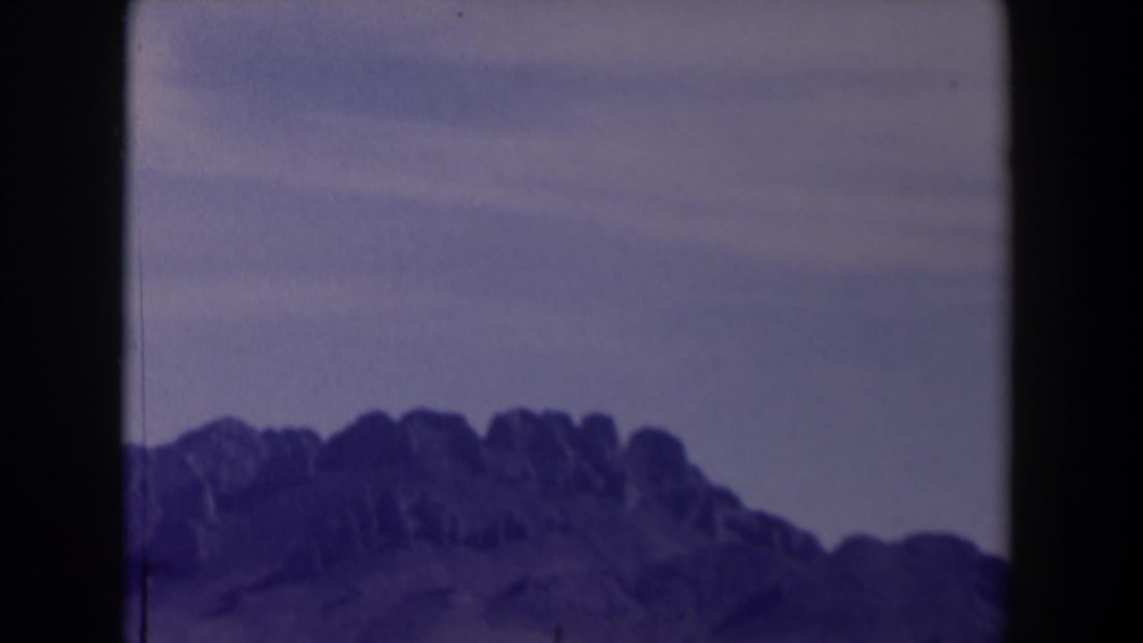 1958 Texas 8mm frame showing a distant rugged ridge beneath a pale hazy sky, with dark film borders and aged color cast.