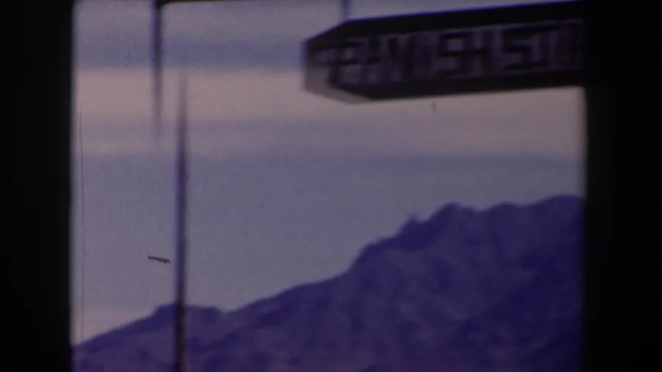 1958 Texas 8mm frame showing a hanging Spanish Stirrup sign over distant blue-purple mountains and a pale sky.