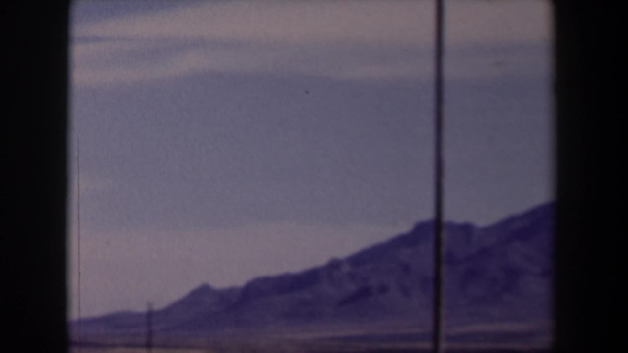 1958 Texas home-movie frame showing distant rugged mountains through a vehicle window, with dry terrain and a faded purple cast.