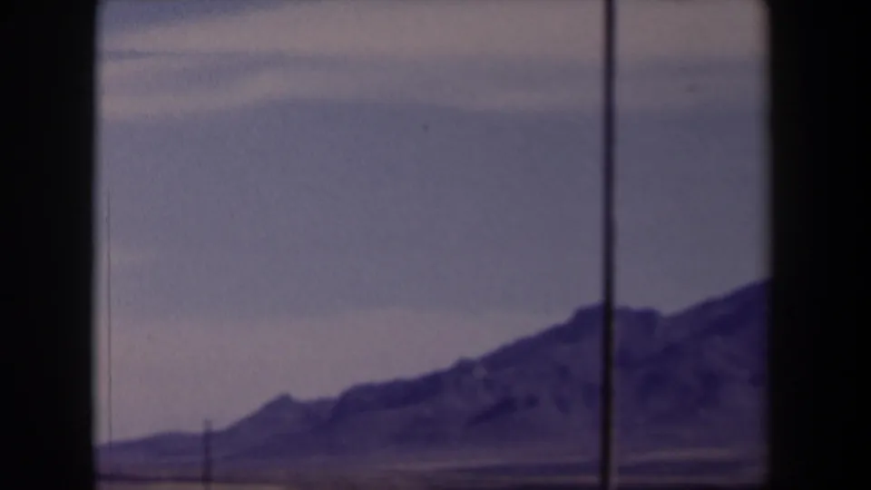 1958 Texas home-movie frame showing distant rugged mountains through a vehicle window, with dry terrain and a faded purple cast.