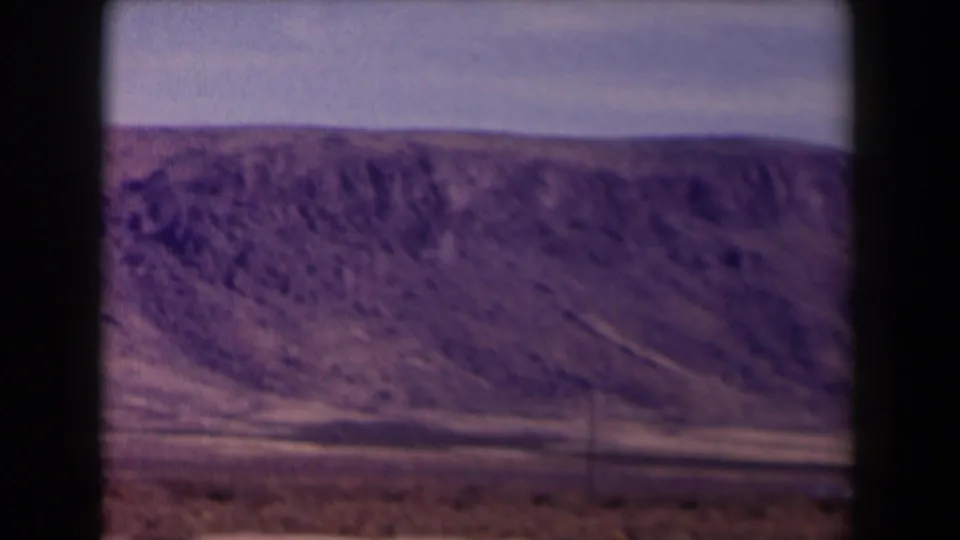 Texas road-trip footage shows a rocky hillside across a dry plain, with window bars and aged 8mm color visible in the frame.