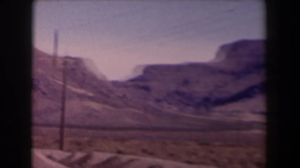 1958 Texas 8mm frame of arid hills and a visible utility pole beside a road or track through open terrain.