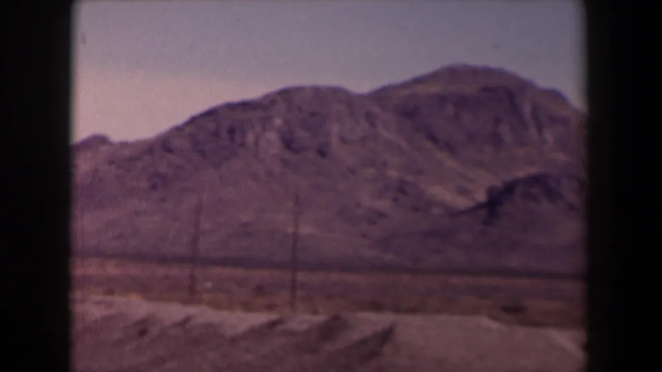 1958 Texas 8mm frame showing low arid mountains, open scrubland, and faint roadside utility lines.