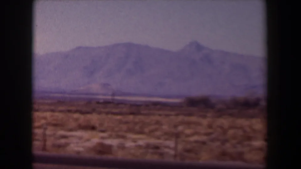 1958 Texas 8mm frame showing open desert terrain, low scrub, a distant mountain range, and soft faded color.