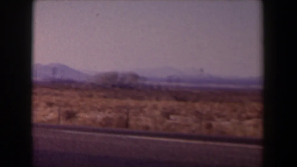 1958 Texas road-travel frame with open scrubland, distant mountains, pale sky, and dark film-frame borders.