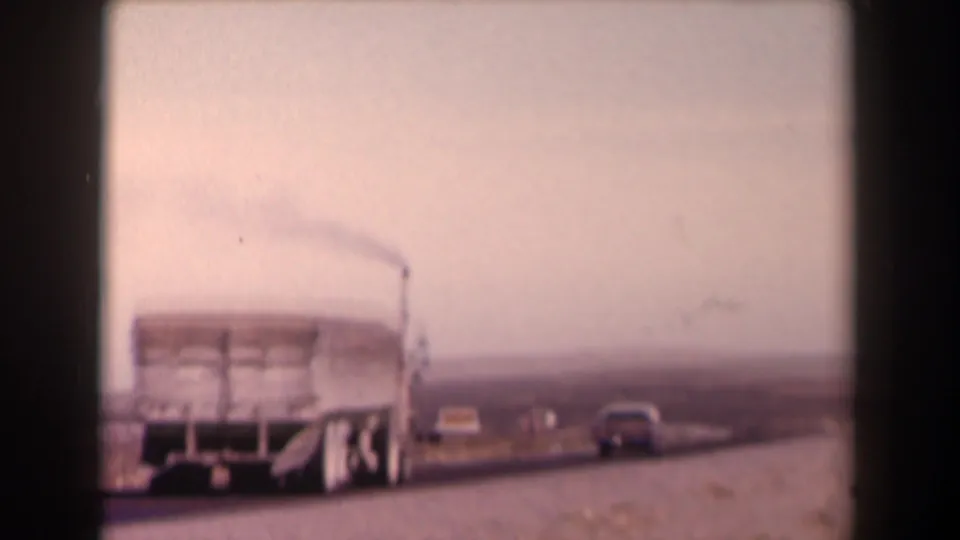 1958 Texas highway frame showing a white cargo truck ahead, cars nearby, open roadside terrain, and a hazy sky.