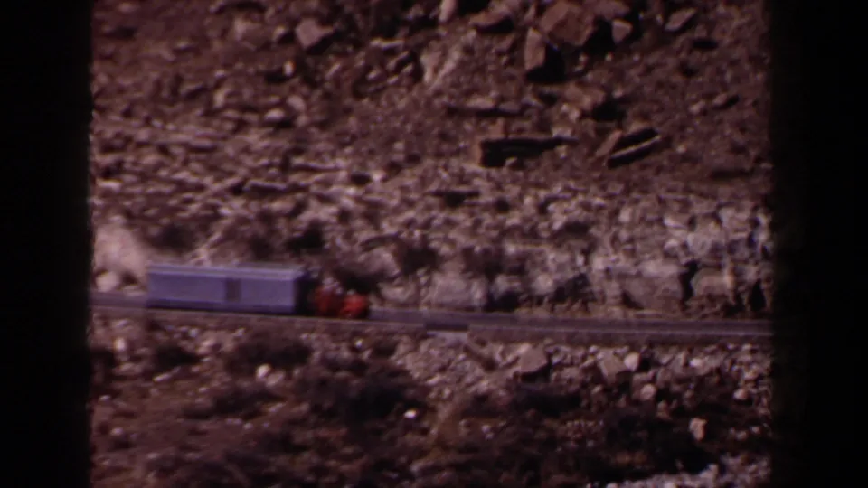 1958 Texas 8mm frame showing a red-and-gray big rig passing below a rocky embankment on a rural road.