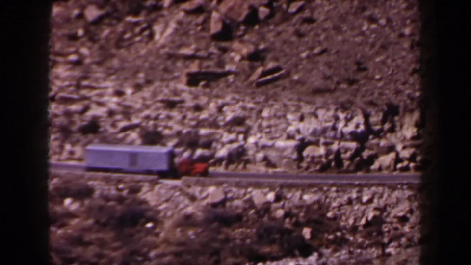 1958 Texas 8mm frame showing a red truck cab pulling a white trailer along a narrow rocky mountain road.