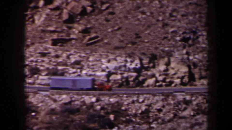 A 1958 Texas home-movie frame shows the truck lower in view, moving past boulders and pale rock along the desert road.