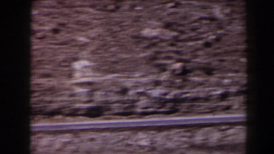 Soft 8mm view of a paved road at the base of a rocky Texas slope as the camera moves past.