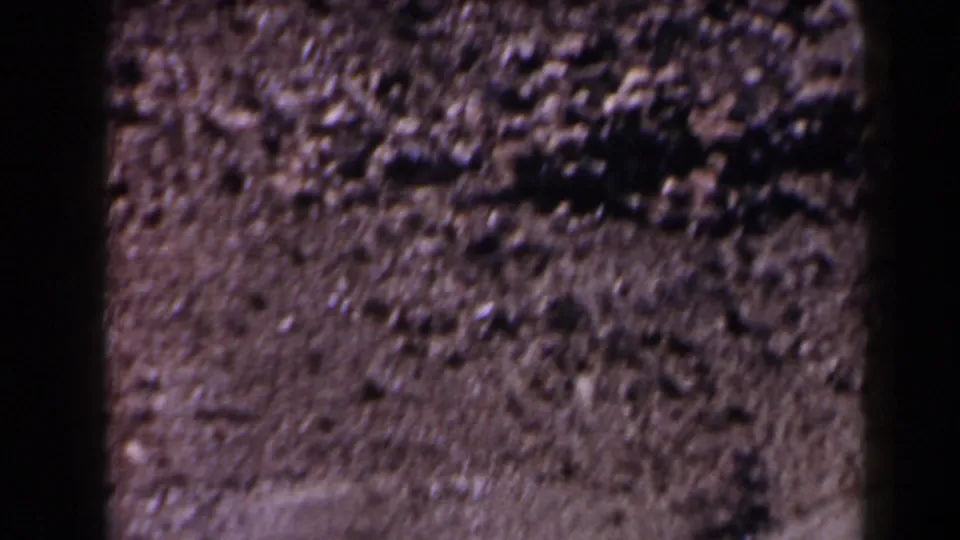 Moving 8mm frame of rocky roadside ground in Texas, with soft focus and visible film texture.