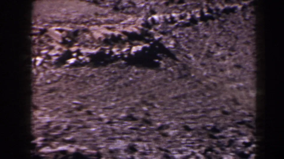 1958 Texas home-movie frame showing rough rocks, dry ground, and a sloped roadside landscape.