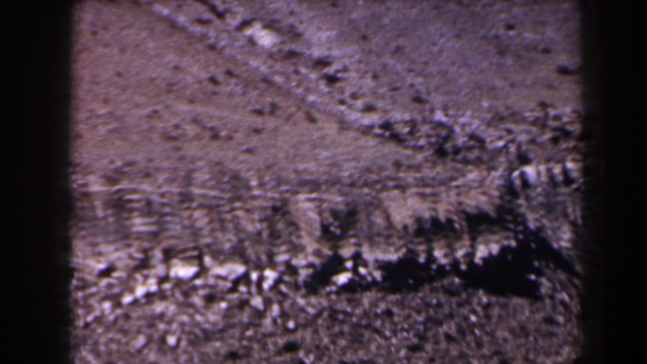 1958 Texas 8mm frame showing rocky dry earth, rough ground texture, and dark vertical film-frame edges.