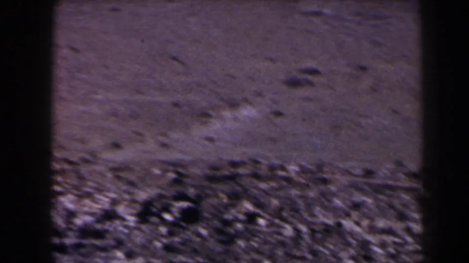 1958 Texas 8mm frame of flat barren terrain with scattered stones, soft focus, and dark frame edges.