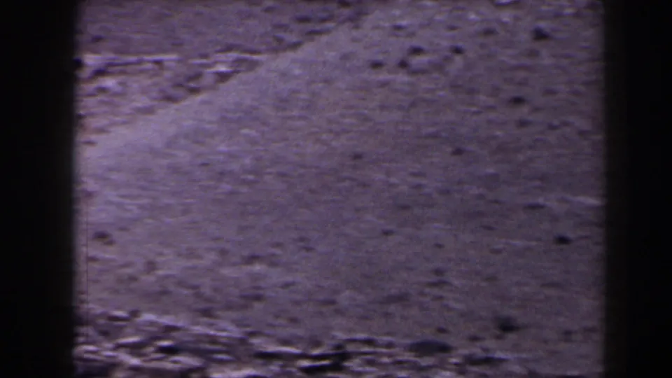 1958 Texas 8mm frame showing open dry field surface, scattered stones, and a rough foreground strip.