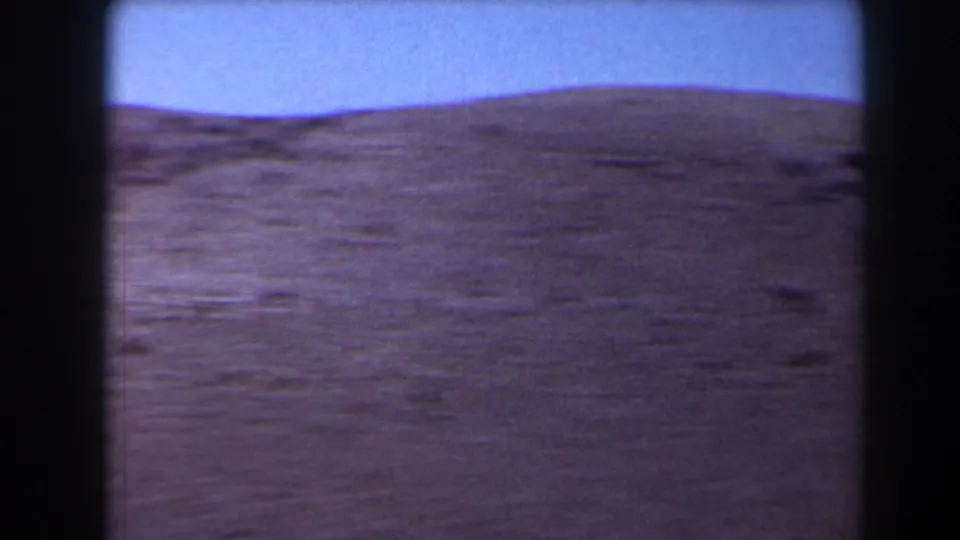 1958 Texas 8mm frame of an empty open field under pale blue sky, with a low distant rise on the horizon.