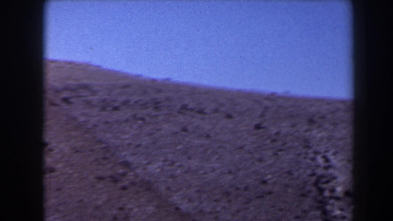 1958 Texas 8mm frame showing a close view of a brown hill slope under clear blue sky with grain and dark edge framing.