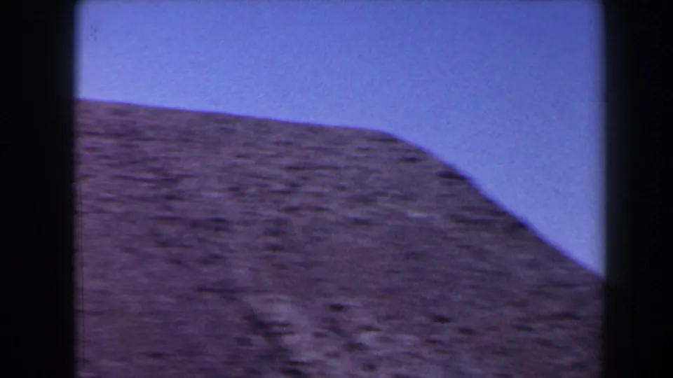 1958 Texas home-movie frame of a rounded brown hilltop set against blue sky, with visible grain and contact-sheet borders.
