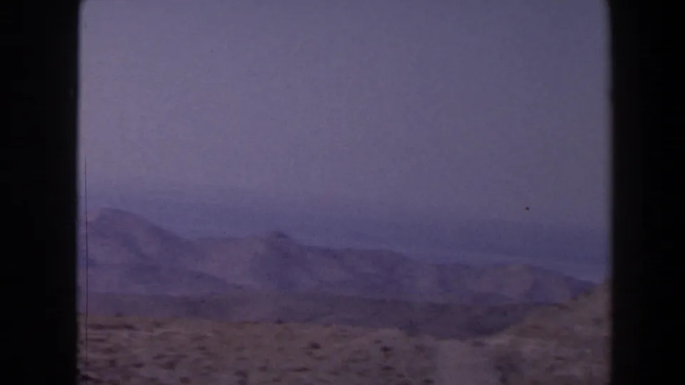 1958 Texas 8mm frame showing distant low mountains beyond arid ground, with a hazy blue sky and vintage color shift.