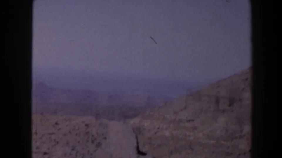 1958 Texas 8mm frame showing a brown hillside, distant open fields, and a hazy overcast sky from a high vantage point.