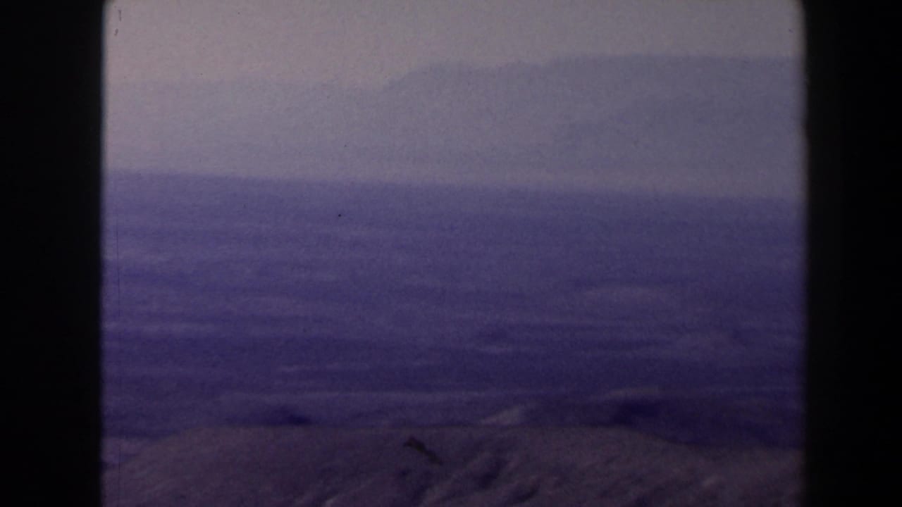 1958 Texas 8mm frame showing a hazy mountain-top view across dry hills, distant ridges, and a muted sky.