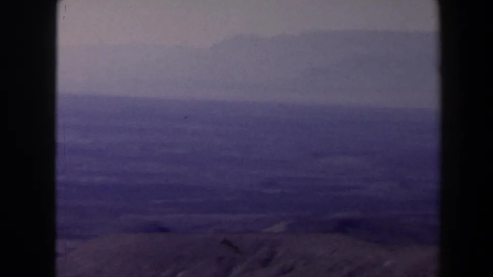 1958 Texas 8mm frame showing a hazy mountain-top view across dry hills, distant ridges, and a muted sky.