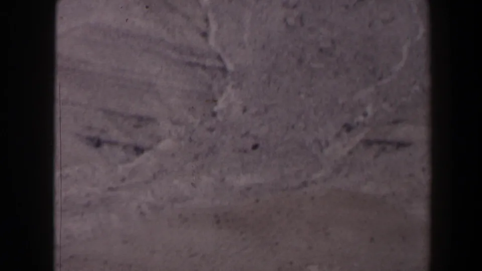 1958 Texas 8mm frame showing a close, soft-focused view of weathered gray rock with cracks and surface marks.