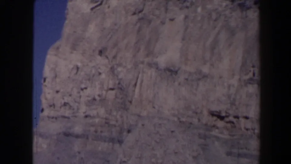 1958 Texas 8mm frame showing part of a rugged gray rock formation with blue sky at the side.