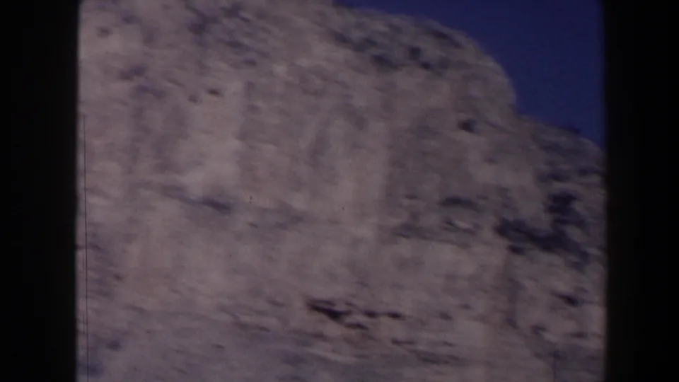 1958 Texas home-movie frame of a rough gray rock ledge, softly focused against deep blue sky.