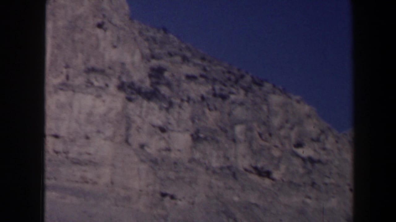 Rocky cliff face beneath a deep blue sky, bordered by dark film edges.