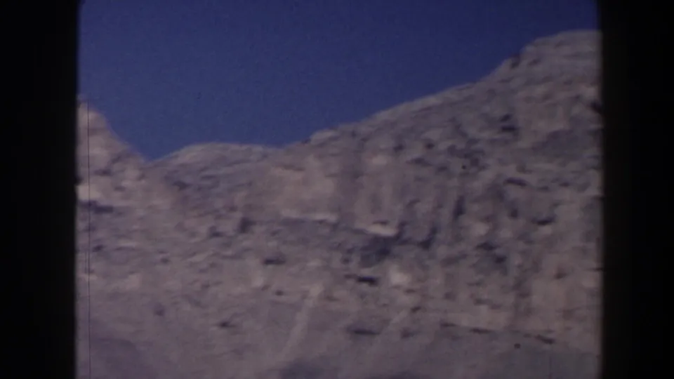 1958 Texas 8mm frame of a bare mountain ridge with textured rock faces under blue sky.