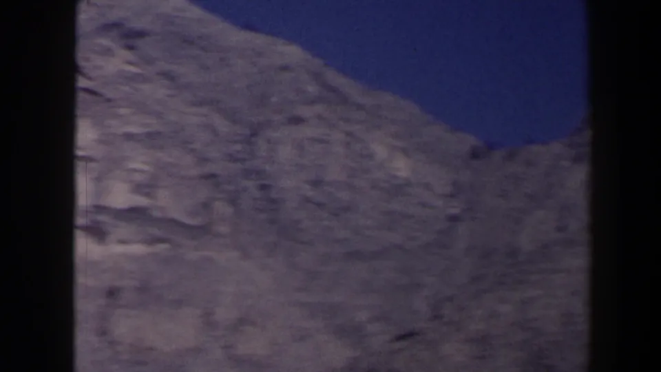 1958 Texas 8mm frame showing sloped arid rock terrain and a low ridge beneath blue sky.