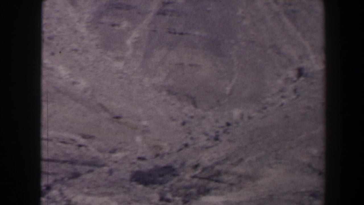 Rugged desert slope with pale ground, dark patches, and film borders.
