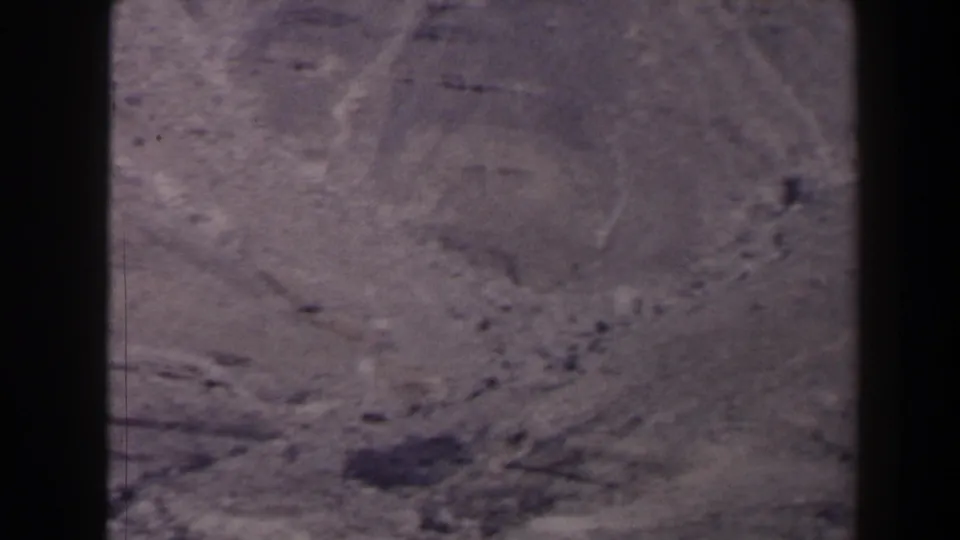 1958 Texas 8mm frame of rugged desert ground and rocky patches viewed from an elevated position, tinted brown-purple by the film scan.