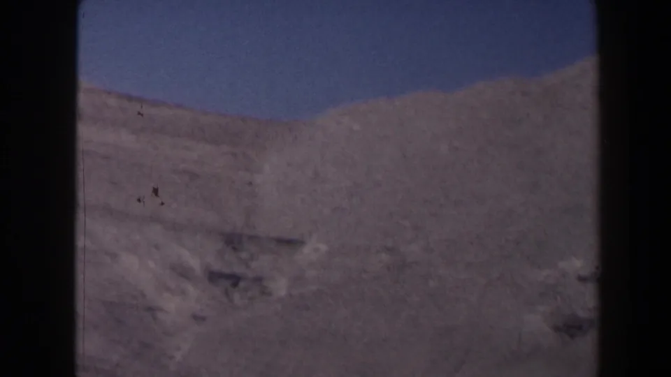 1958 Texas 8mm frame showing a pale rocky canyon slope or mountain face under clear sky, with heavy film border visible.