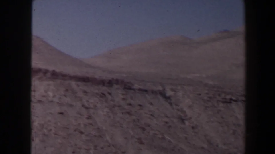1958 Texas 8mm view across rugged canyon terrain toward rounded mountain ridges beneath a clear blue sky.