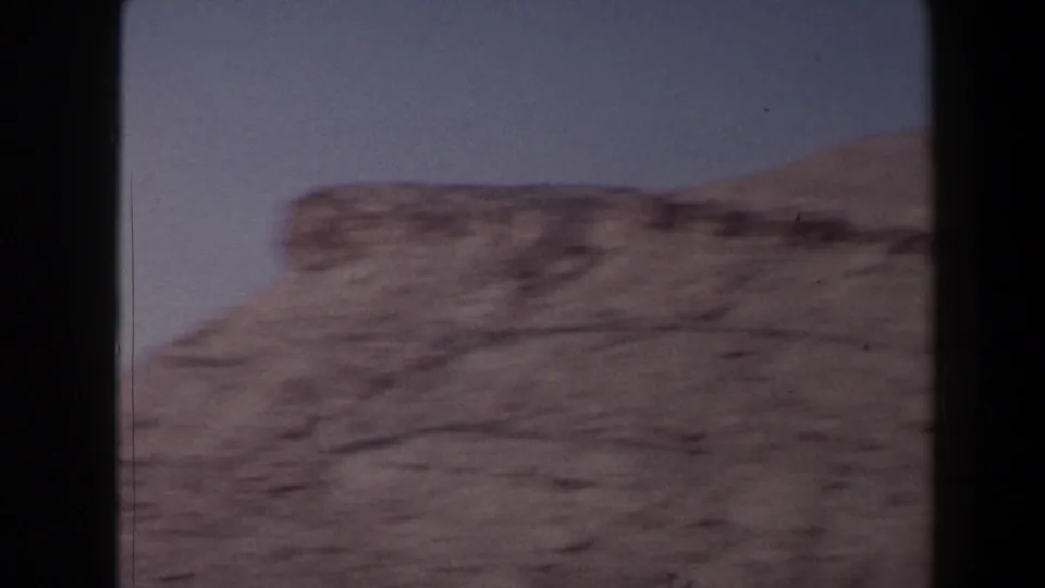 Handheld 1958 Texas 8mm frame with a blurred rocky bluff and arid slope, suggesting camera movement across canyon terrain.