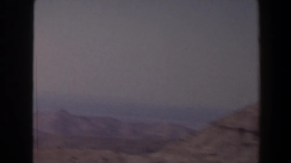 1958 Texas 8mm landscape frame with soft distant mountain forms, rocky foreground slopes, and open sky in muted color.