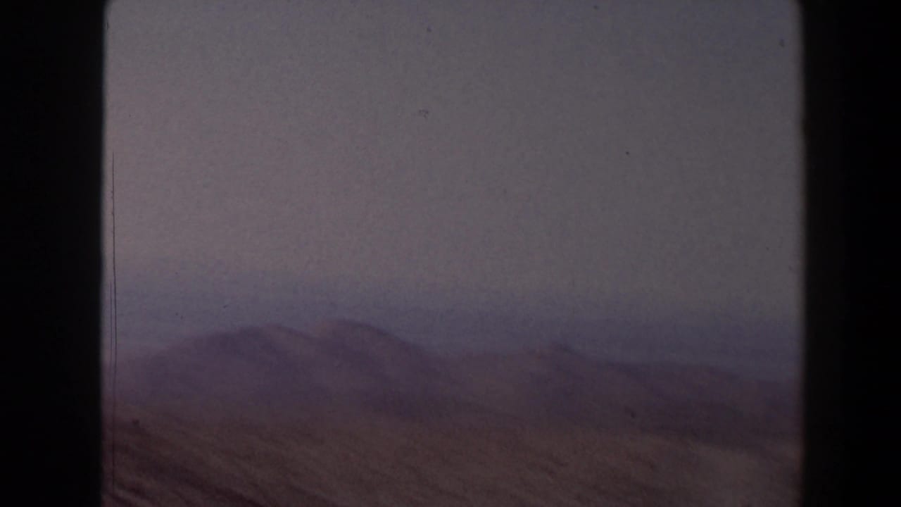 Distant desert hills and scrub seen through dark 8mm frame borders.