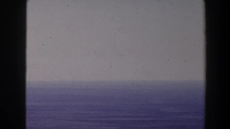 Home-movie frame showing a hazy body of water and distant horizon, with soft exposure and dark 8mm frame edges.