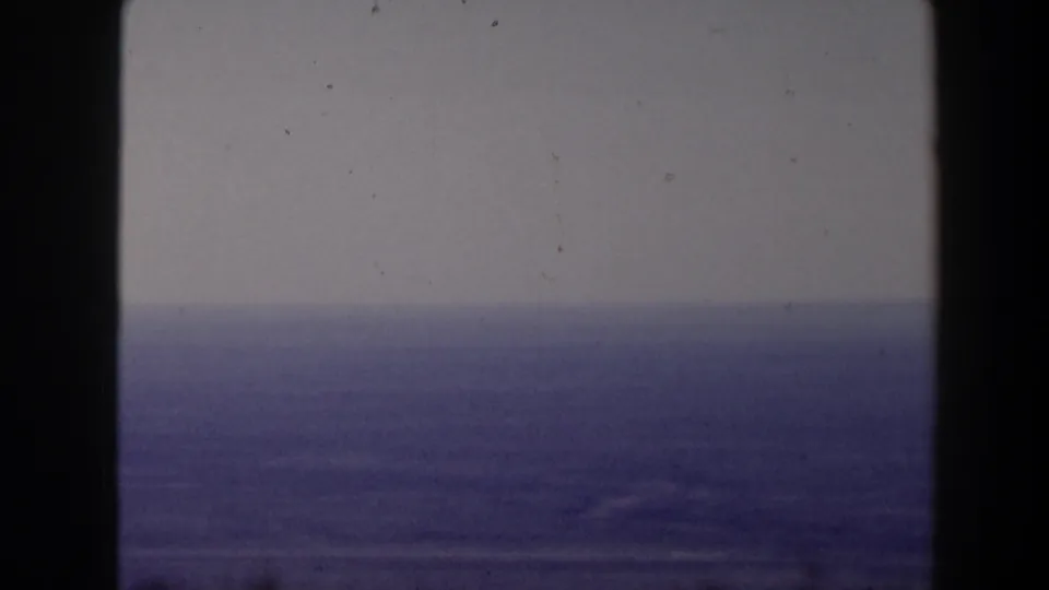 1958 home-movie frame of a broad water view and hazy horizon, with visible grain and vertical film-frame borders.