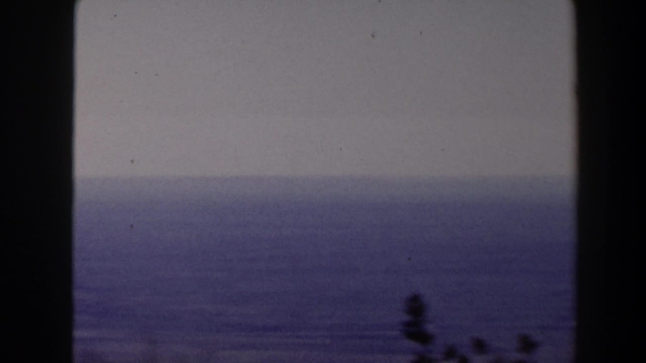1958 Texas 8mm frame showing a calm blue seascape under a pale sky, partly divided by a dark window or structural edge.