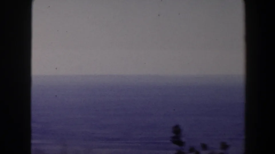 1958 Texas 8mm frame showing a calm blue seascape under a pale sky, partly divided by a dark window or structural edge.