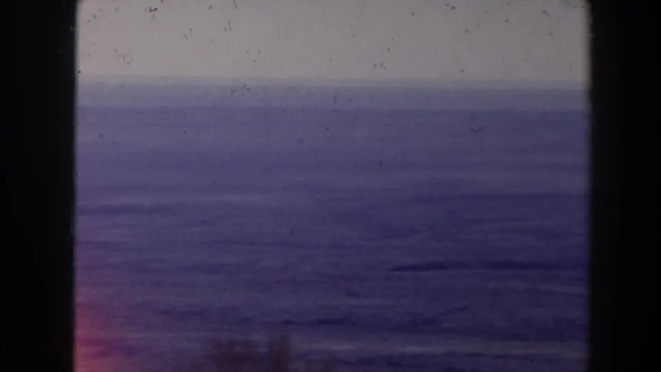 1958 Texas archival 8mm view of calm blue water and a pale horizon, with a dark frame edge and light film wear visible.